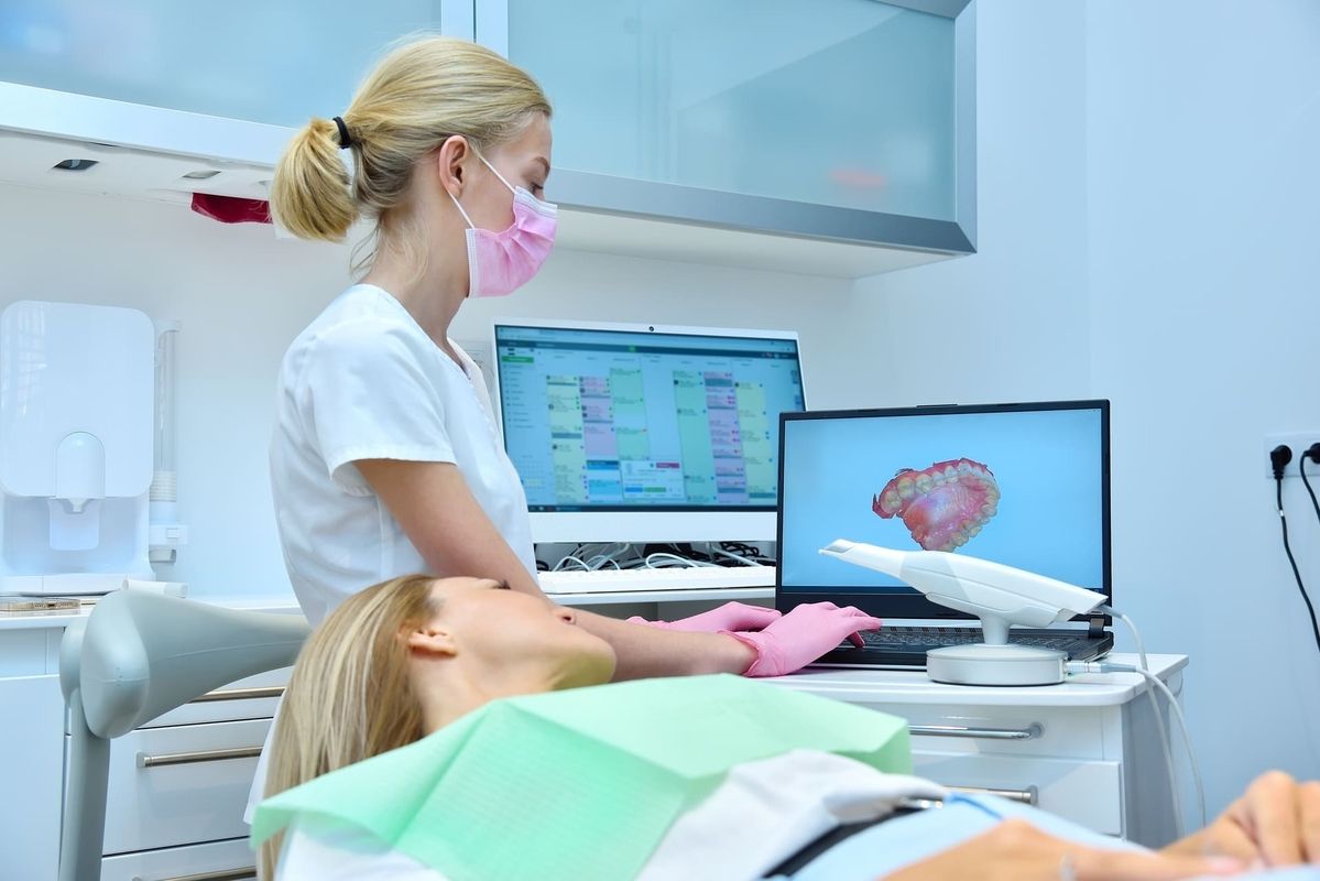 A woman in a dentist's office stands next to a patient sitting in the treatment chair